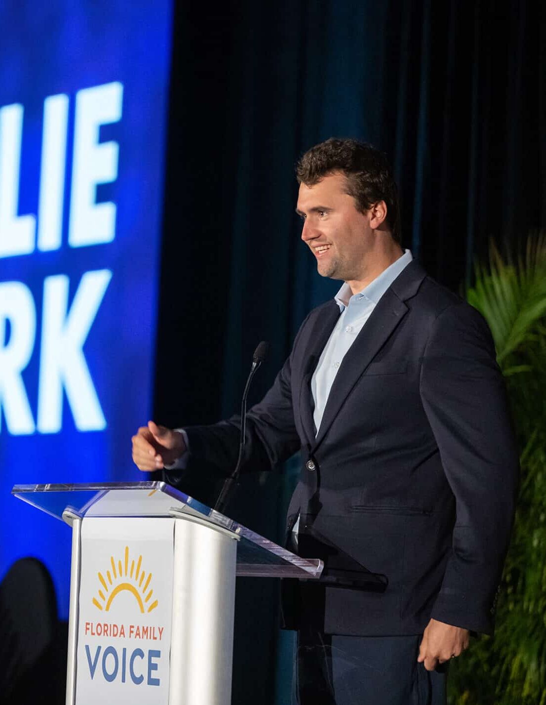 Charlie Kirk speaks at a podium labeled “Florida Family Voice,” with a large screen behind him displaying “CHARLIE KIRK” and his image.